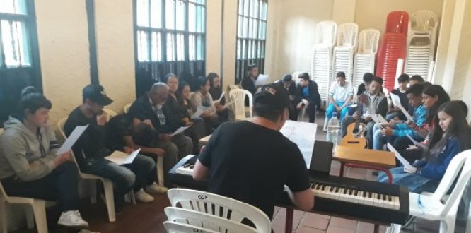 Foto de jóvenes en un salón con una persona que toca el piano